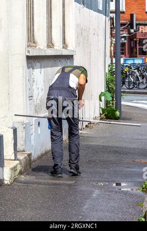 Male worker cutting metal angle with saw incorrectly using knee as support - Paris, France. Stock Photo