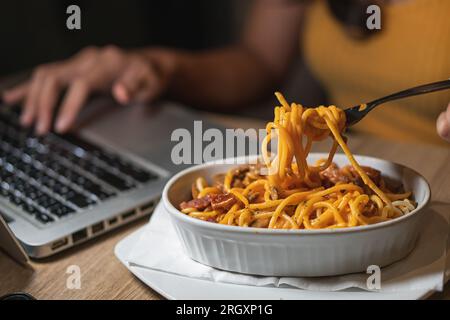 Eating spaghetti while working on laptop at home. Unhealthy food during conference call, meeting. Stock Photo