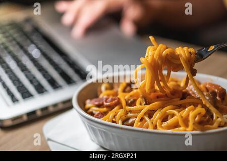 Eating spaghetti while working on laptop at home. Unhealthy food during conference call, meeting. Stock Photo