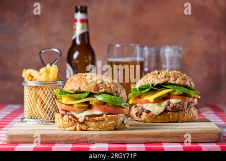 Two homemade cheese burgers on wood board with fries and glass of beer Stock Photo