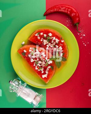 Grilled watermelon with feta cheese, chili pepper and min on olive color plate over on green red background. BBQ healthy food concept. Food geometry Stock Photo