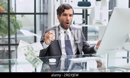 Shocking news. Surprised young man in a suit and tie looking at a laptop while sitting at his workplace Stock Photo
