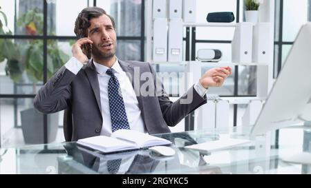 young web developer talking on phone while working with laptop in office Stock Photo