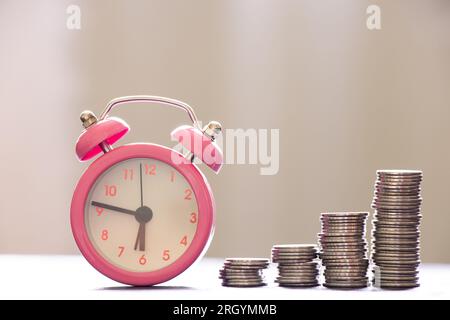 Stacks of coins stand on a wooden table and an alarm clock stands nearby, business and finance, success time Stock Photo