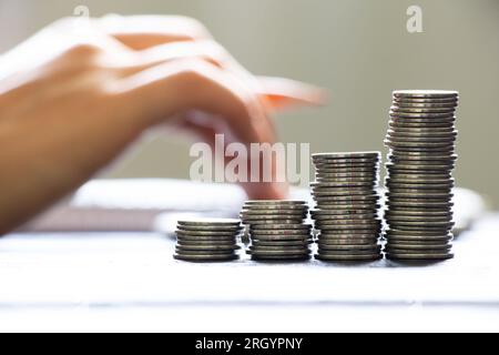 A hand on a calculator and next to it lies a notebook and stacks of coins, business and finance Stock Photo