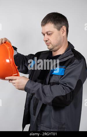 A man in overalls holds a builders helmet in his hands on a white background Stock Photo