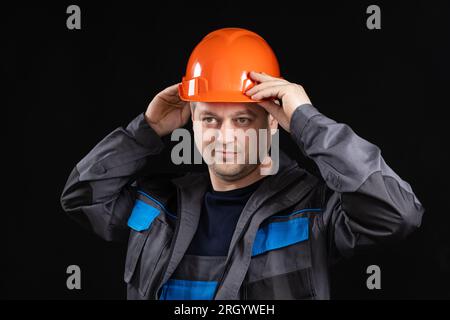 A young man construction worker in a safety helmet and work uniform on a black background Stock Photo