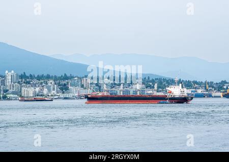 A large oceangoing ship is guided into the Port of Vancouver by tug boats. Stock Photo