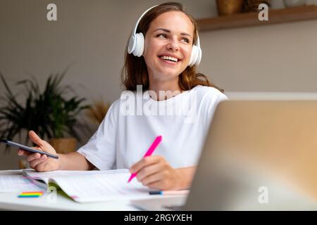Young female university  student listens to educational audio records using her wireless headphones and her smart phone. Stock Photo