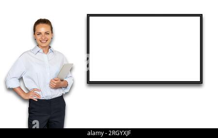 Young smiling businesswoman wearing trousers and shirt standing next to big digital display on the white wall. Stock Photo