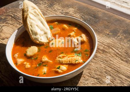 A bowl of fish stew or bouillabaisse, that has been made with king scallops, smooth hound, anglerfish also known as monkfish and gurnard fillets. Serv Stock Photo