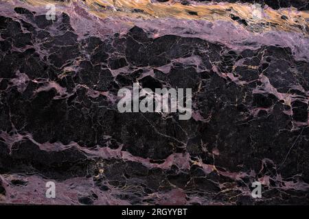Close-up texture of a black marble formation with pink and orange streaks. The background is a dark, solid color. Stock Photo