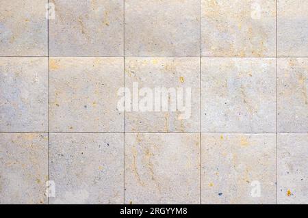 A tiled wall with square, beige tiles and thin, white grout lines. Stock Photo