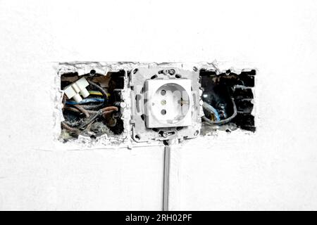 Broken defective damaged wall sockets with uncovered wires close up. Incomplete defective old mains outlet Stock Photo