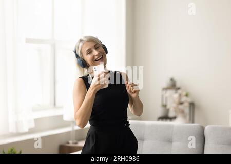 Happy mature woman dancing at home with wireless headphones Stock Photo
