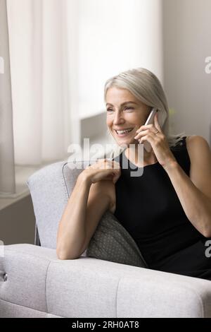 Positive blonde mature woman talking on smartphone at home Stock Photo