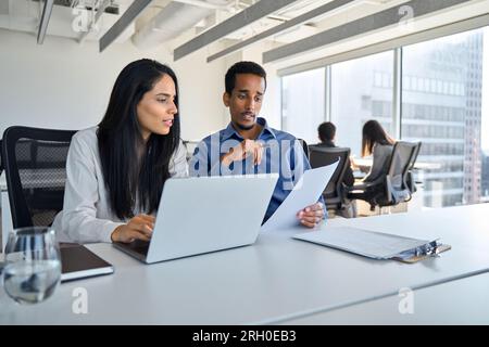 Diverse employees using laptop discussing business documents working in office. Stock Photo