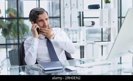 young web developer talking on phone while working with laptop in office Stock Photo