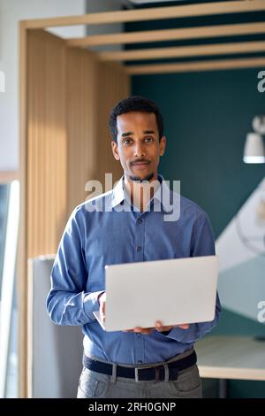 Professional business man standing in office with laptop. Vertical portrait. Stock Photo