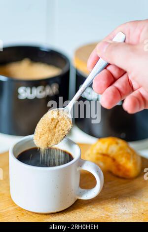 Grains of brown sugar drop from a spoon,about to be srirred into a freshly brewed black espresso,ready to drink,hot and sweet at breakfast time,a brea Stock Photo