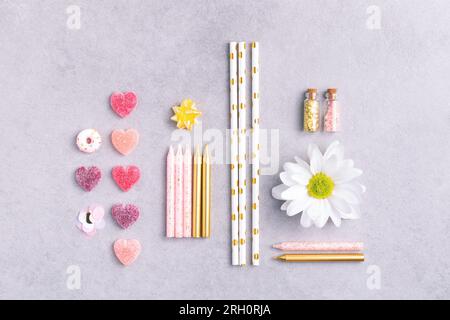 Birthday party background. Knolling composition with sweet hearts, flower, pink and golden birthday candles, confetti and paper straws on grey table. Stock Photo