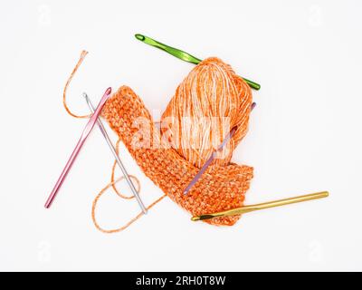 On a white background, there's pumpkin-colored yarn alongside multiple crochet hooks in assorted colors, all isolated. Stock Photo