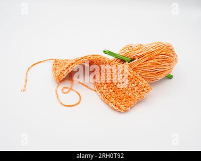 Isolated on a white background, there's pumpkin-colored yarn paired with a green crochet hook. Stock Photo