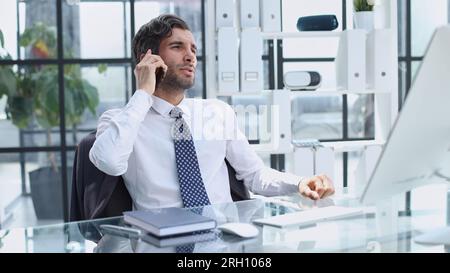 young web developer talking on phone while working with laptop in office Stock Photo