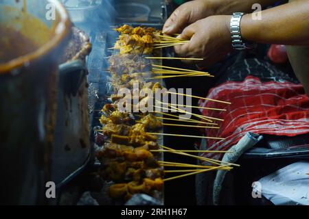 The scene of Sate Padang, a type of Indonesian skewered and grilled meat dish, being cooked over an open flame at a street food stall. Stock Photo