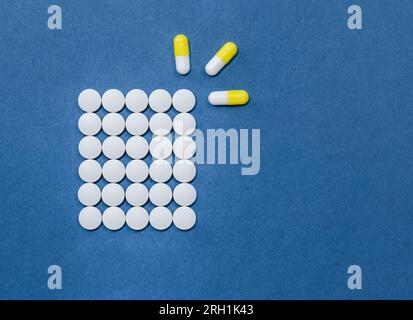 White and yellow pills on a blue background. Stock Photo