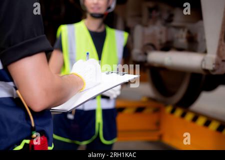 Closeup hands engineer man and woman or worker checking electric train for planning maintenance writing document on clipboard in station, transport an Stock Photo