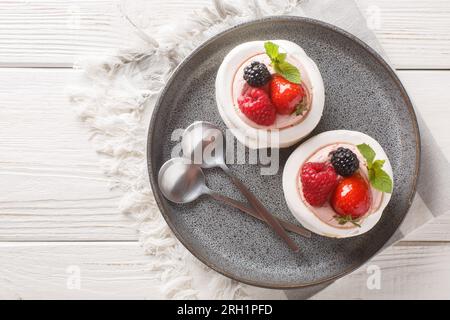 Tasty Pavlova meringue cakes with fresh berries on a plate on the wooden table. Horizontal top view from above Stock Photo