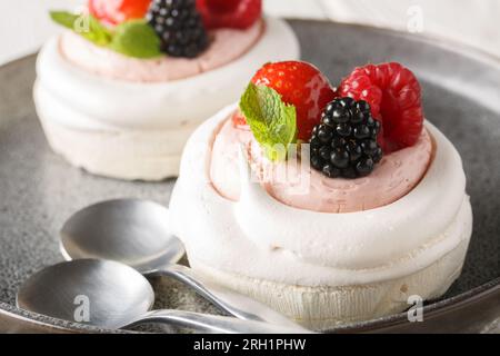 Tasty Pavlova meringue cakes with fresh berries on a plate on the wooden table. Horizontal Stock Photo