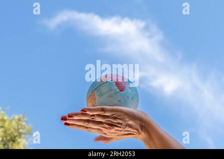 A female hand holds a globe against the blue sky Stock Photo