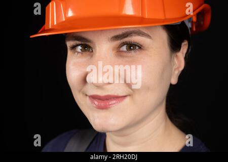 A female construction worker or engineer wearing a protective orange mask on a black background Stock Photo