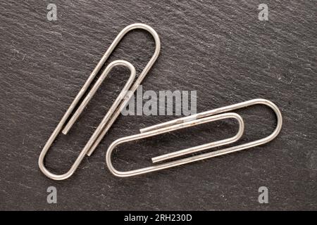 Two metal paper clips on slate stone, macro, top view. Stock Photo