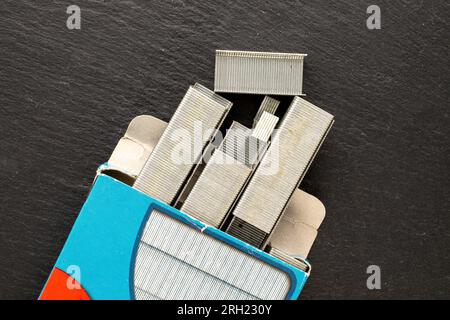 Several metal stapler staples in a paper box on slate stone, macro, top view. Stock Photo