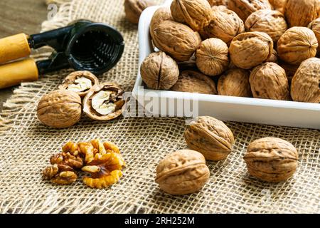 Walnuts on a white tray, some cracked walnuts on burlap fabric and a nutcracker. Stock Photo