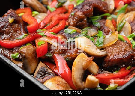Stewed veal with vegetables and mushrooms in a frying pan on a black background Stock Photo