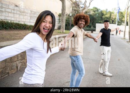 Three diverse and confident friends holding hands together. Multiracial group of people laughing and holding hands in a line. Focus on first woman. Stock Photo