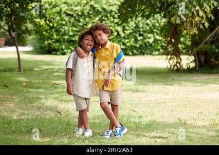 Brothers with backpacks standing on school backyard, hugging and looking at camera Stock Photo