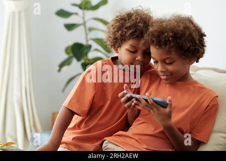 Siblings watching entertaining video on smartphone when sitting on couch at home Stock Photo