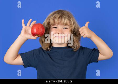Little boy holding apple with fynny face. Kid eats healthy food. Stock Photo