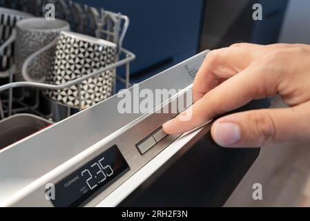 Man pushing start button on the control panel of the dishwasher. Stock Photo