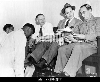 Lieutenant Commander ROBERT MONTGOMERY (returning to the studio after 4 years combat service) and BUSTER KEATON (at the time a writer for MGM) have their shoes shined on the MGM Studios Lot in Hollywood in late 1944 publicity for Metro Goldwyn Mayer Stock Photo