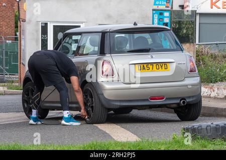 Man at garage petrol station inflating tyres on a mini car using a tyre inflation pump, England, UK Stock Photo