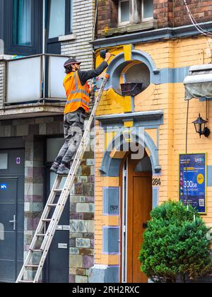 Man on ladder painting brickwork of house - Brussels, Belgium. Stock Photo