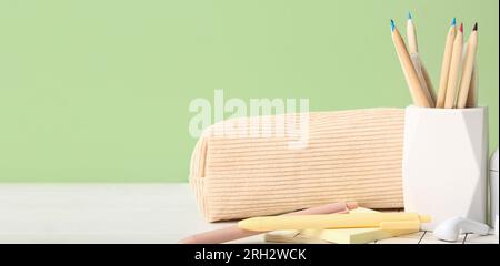 Stylish cup with stationery on table against green background. Banner for design Stock Photo