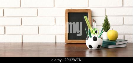 Stylish cup with stationery, chalkboard and apple on table against white brick background. Banner for design Stock Photo
