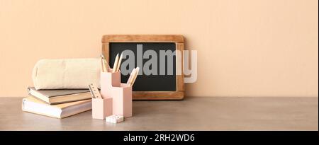 Stylish cup with stationery, books and chalkboard on table against beige background. Banner for design Stock Photo